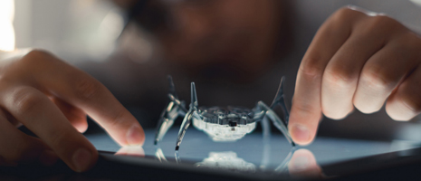Robot spider on a glowing tablet screen, with fingers touching the display.