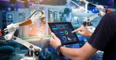 Person using a tablet to control robotic arms in a smart factory.