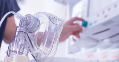 Clear oxygen mask in foreground, hand adjusting medical equipment.