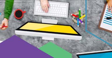Busy design desk with multiple hands, color palette, computer monitors, keyboard, and documents.
