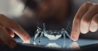 Robot spider on a glowing tablet screen, with fingers touching the display.