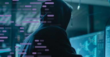 Hacker in a dark hoodie viewing glowing computer screens with data flowing.