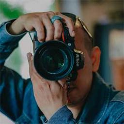 Person holding a Nikon camera, looking through the viewfinder.