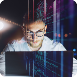 Focused man in glasses working on a laptop at night, with digital code overlay.