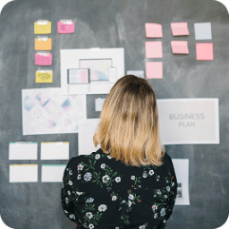 Woman facing a dark wall covered with sticky notes and design documents.
