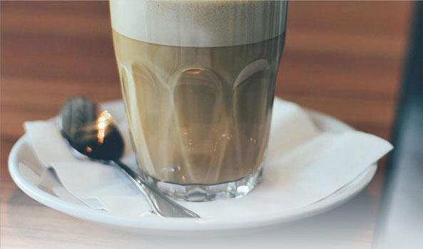 Glass of latte with foam, a spoon, and napkin on a saucer.