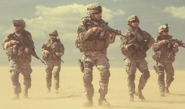 Photograph: Five soldiers in camouflage patrol a sandy, dusty desert.