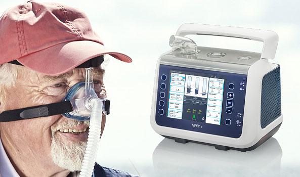 Smiling man with a CPAP mask and a portable respiratory support machine.