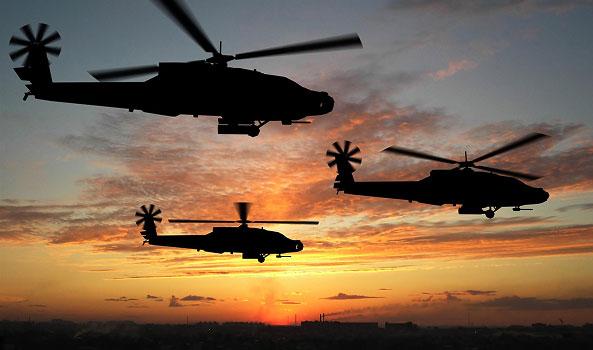 Three military helicopters flying in silhouette at sunset.