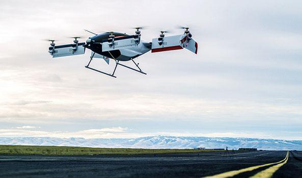 Flying white and black drone above an airstrip with distant mountains.