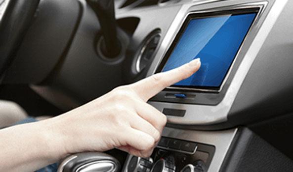 Hand touching a blue touchscreen in a car dashboard.