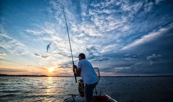 Fisherman on a boat catches a fish jumping from the water at sunset.