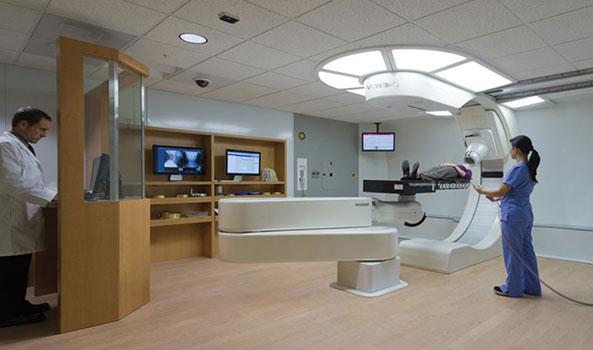 Patient on a medical imaging machine, attended by a doctor and a technician.