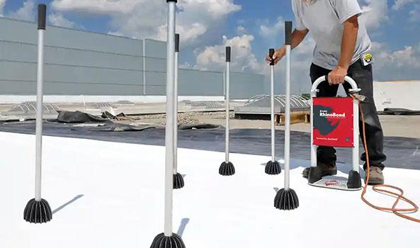 Worker on white roof performing leak detection with a red device and several metal probes.