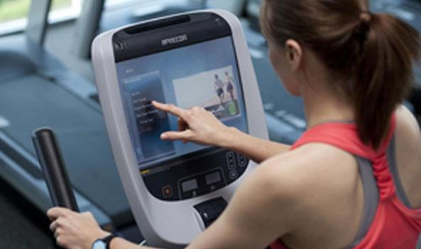 Woman in a red top tapping a Precor exercise machine's touchscreen display.