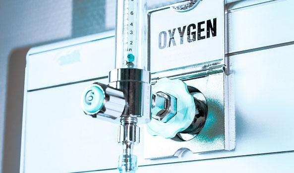 Medical oxygen port on a wall with a chrome valve, flow meter, and 'OXYGEN' label.