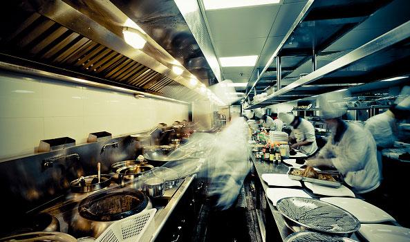 Busy commercial kitchen with chefs cooking and movement blur.