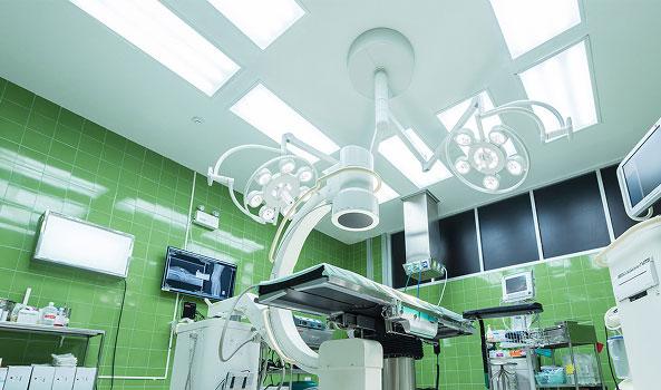 Sterile operating room with surgical table, multiple bright lights, and green tiled walls.