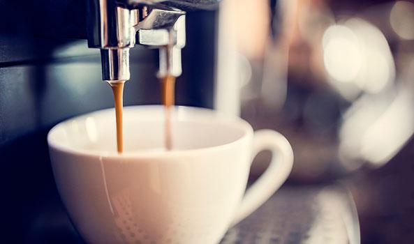 Coffee pouring from an espresso machine into a white cup.